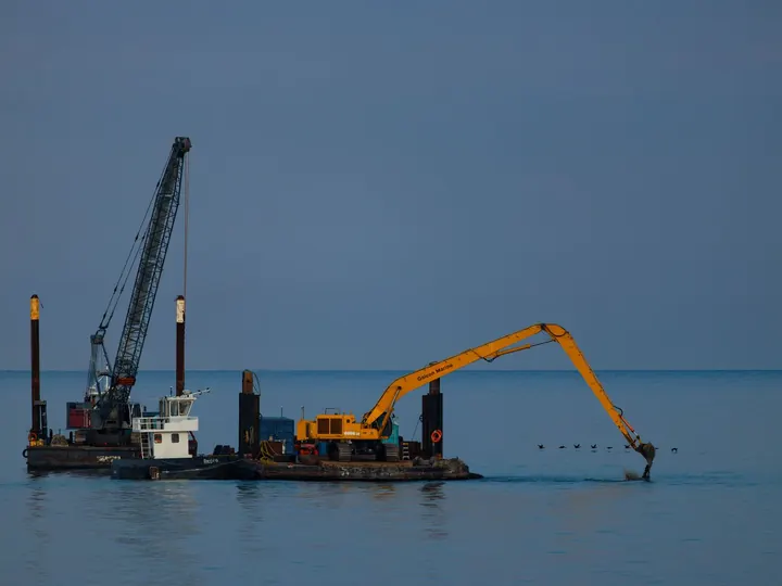 Dredging barge with crane operating at sea under clear sky.