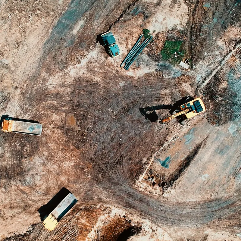 High-angle aerial view of construction site with earthmoving equipment and trucks.