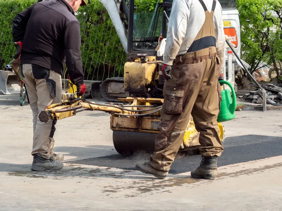 Construction workers using machinery for road repair in Wrocław, Poland.