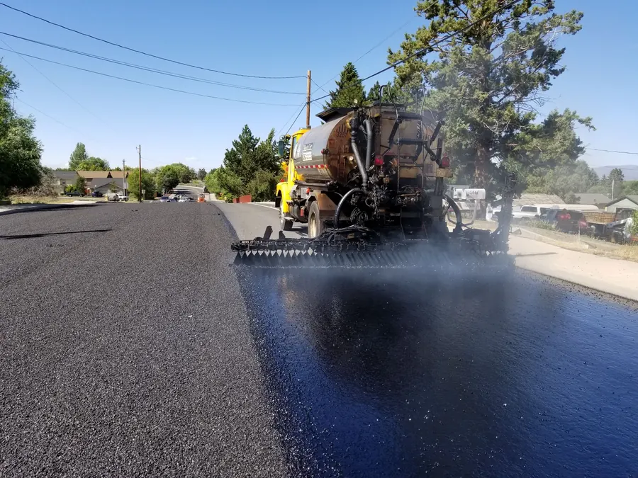 Road construction in Redmond, OR, with asphalt paving equipment. Sunny weather highlights the process.