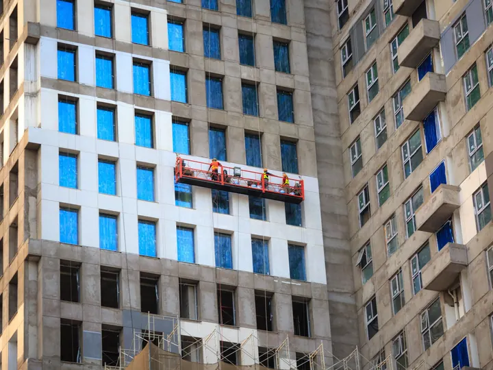 High-rise building construction with workers on a lift, showcasing modern architectural design.