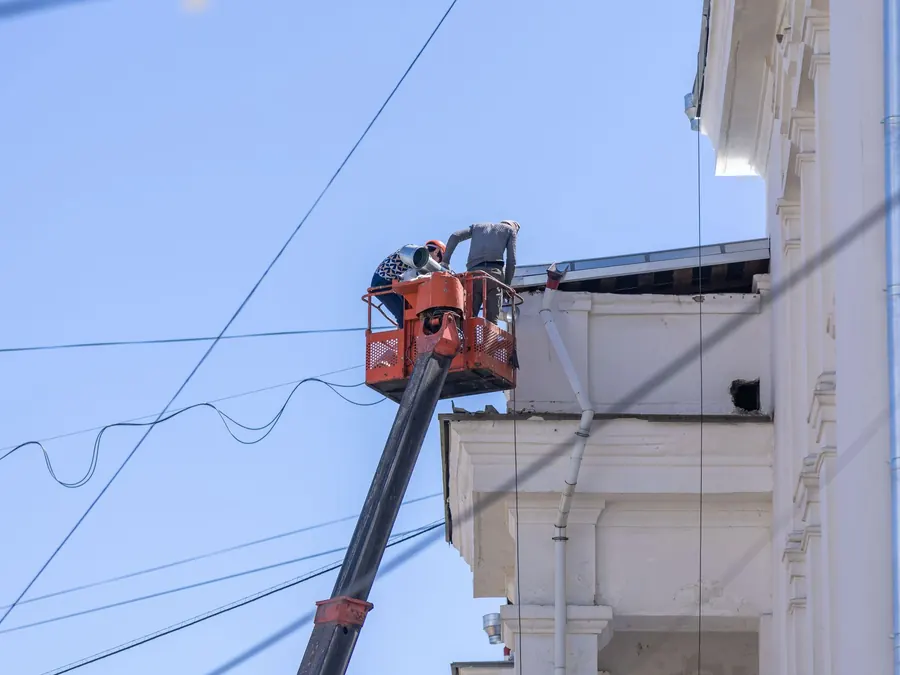 Workers on lift repairing building façade under clear sky.