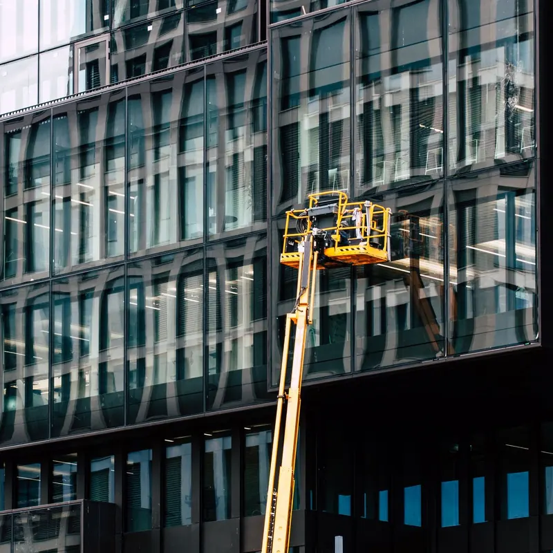 Workers on a lift cleaning windows of a modern glass building exterior.