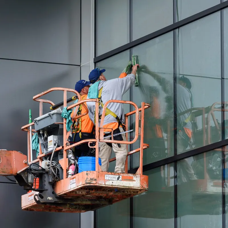 Window cleaners working on a skyscraper using a hydraulic lift in urban setting.