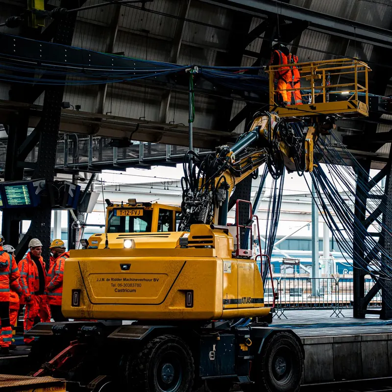 Workers in high-visibility clothing operate machinery at a train station, ensuring safety and efficiency.