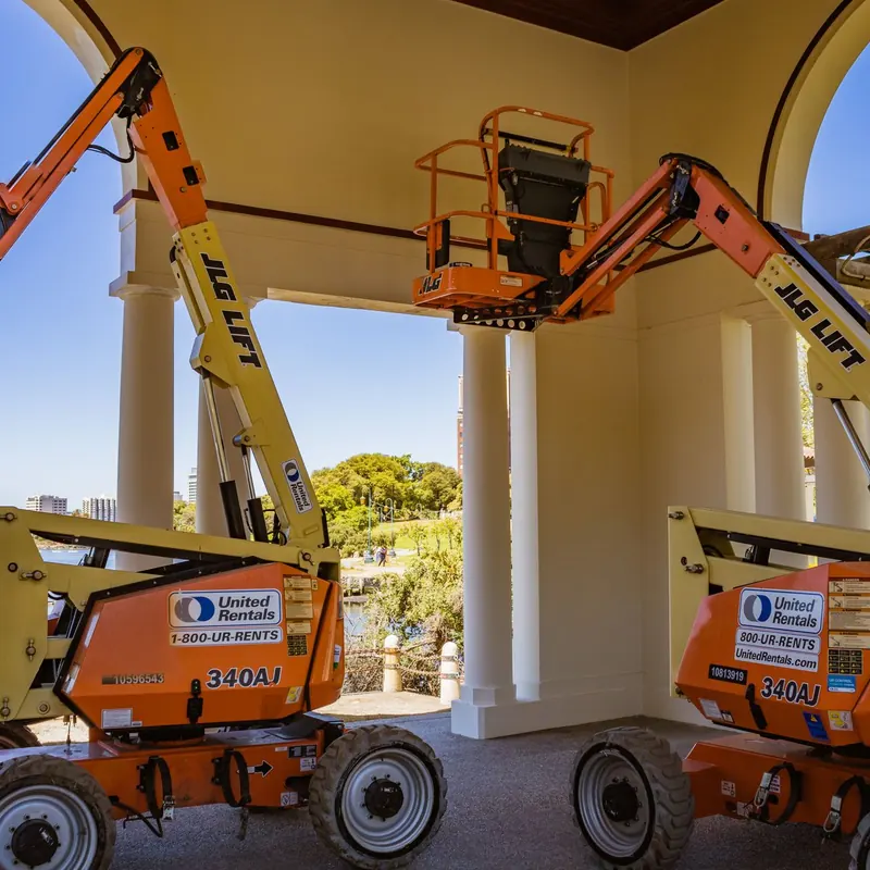 Orange construction lifts positioned near a lakeside with clear sky and architecture.