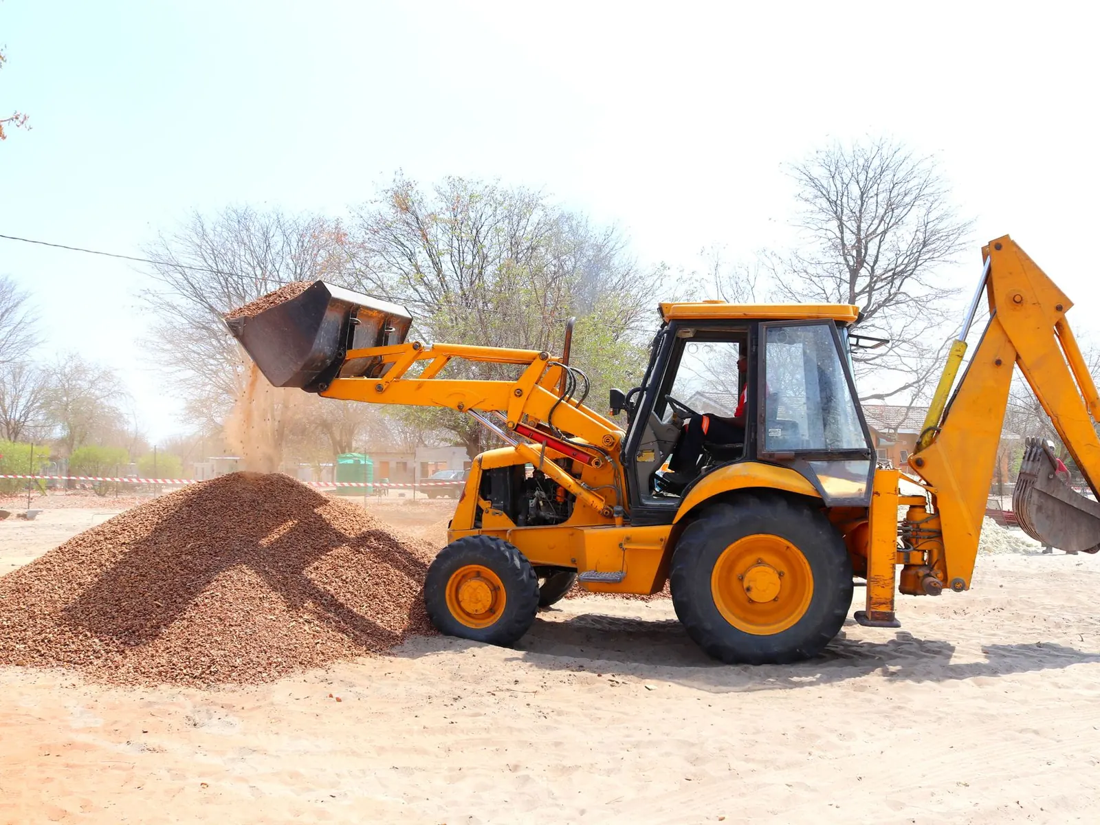 A yellow excavator moving gravel at an outdoor construction site during the day with clear skies.