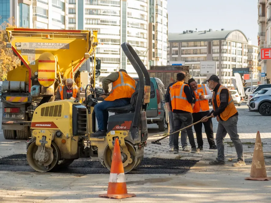 Construction workers in orange vests repair city road with vehicles during the day.