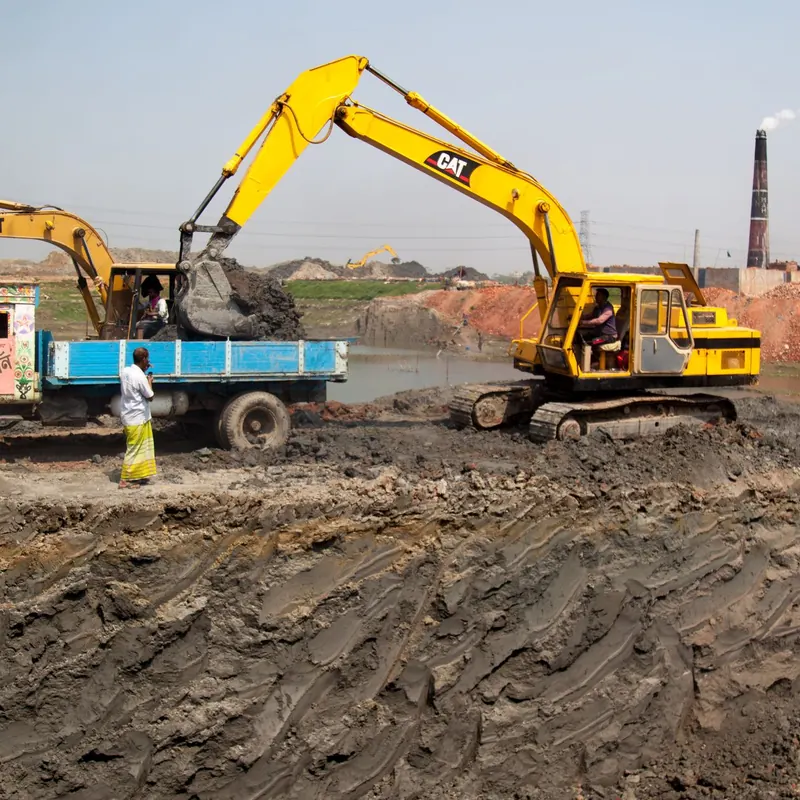 Excavators loading soil into trucks at a construction site in Dhaka, Bangladesh.