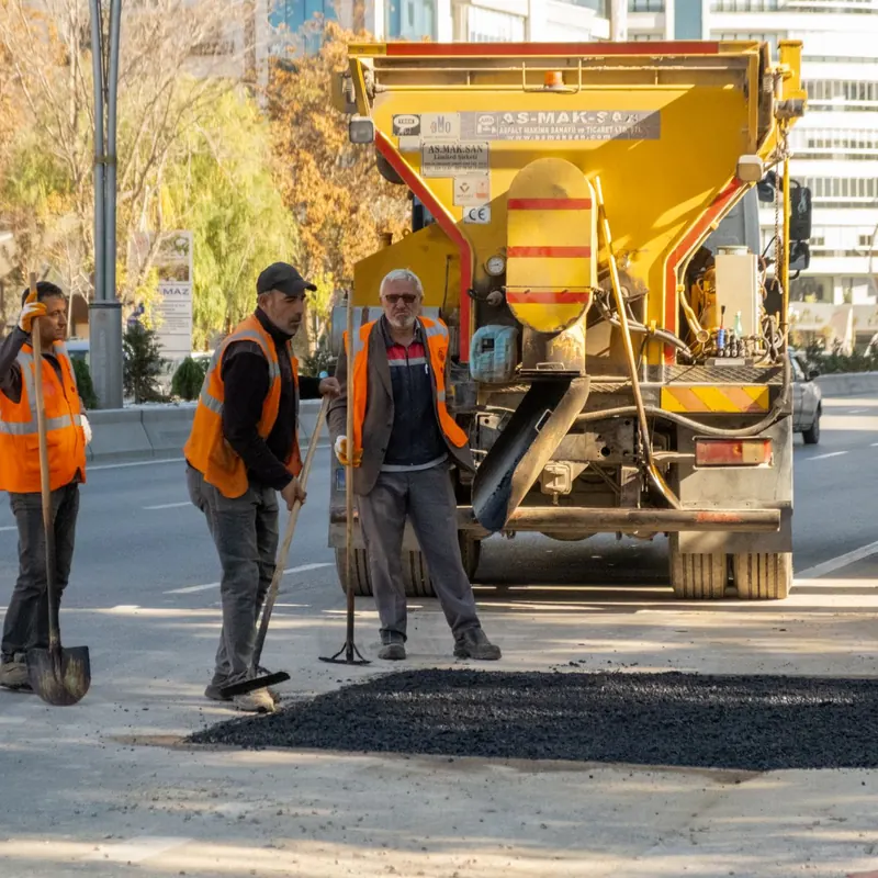 Roadwork crew in orange vests operating machinery on city street, ensuring traffic safety.