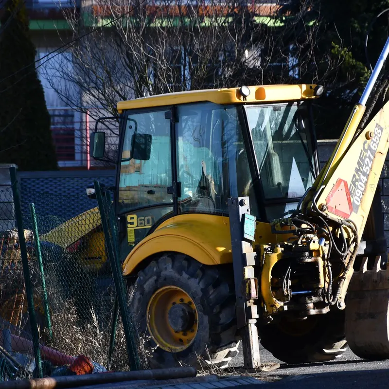 A yellow excavator rests on an urban construction site during daylight.