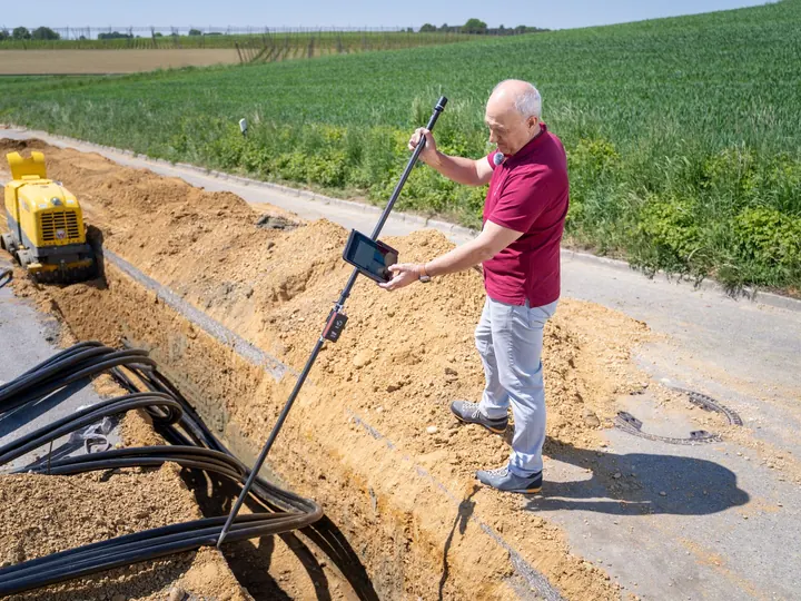 Adult male engineer using surveying equipment at a trench site on a sunny day.