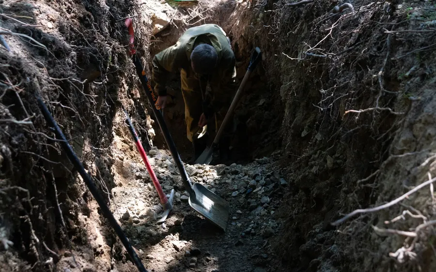 A person digging a trench outside, surrounded by tools and natural surroundings.