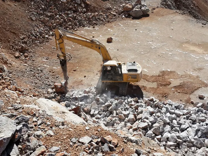 A heavy excavator operating amidst rubble in a sunny Turkish stone quarry, highlighting industrial machinery in action.