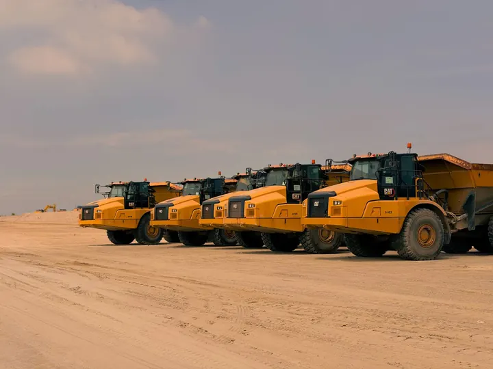 Row of heavy-duty dump trucks parked on a sandy construction site under a clear sky.