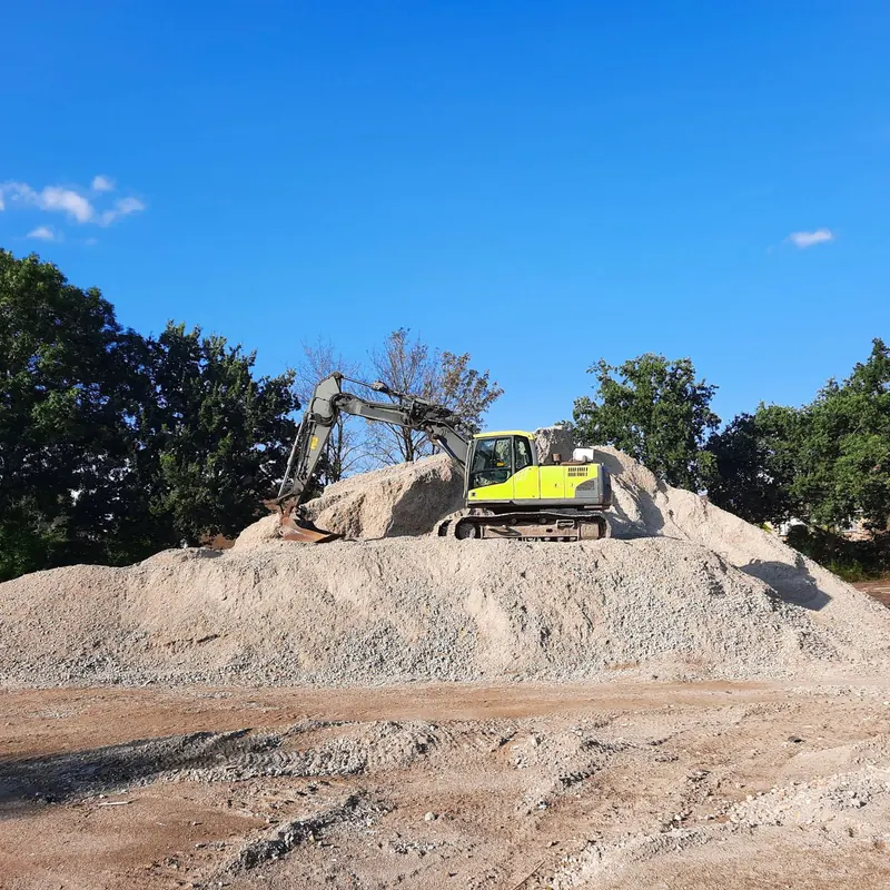 Excavator working on a gravel pile at an outdoor construction site with clear blue sky.